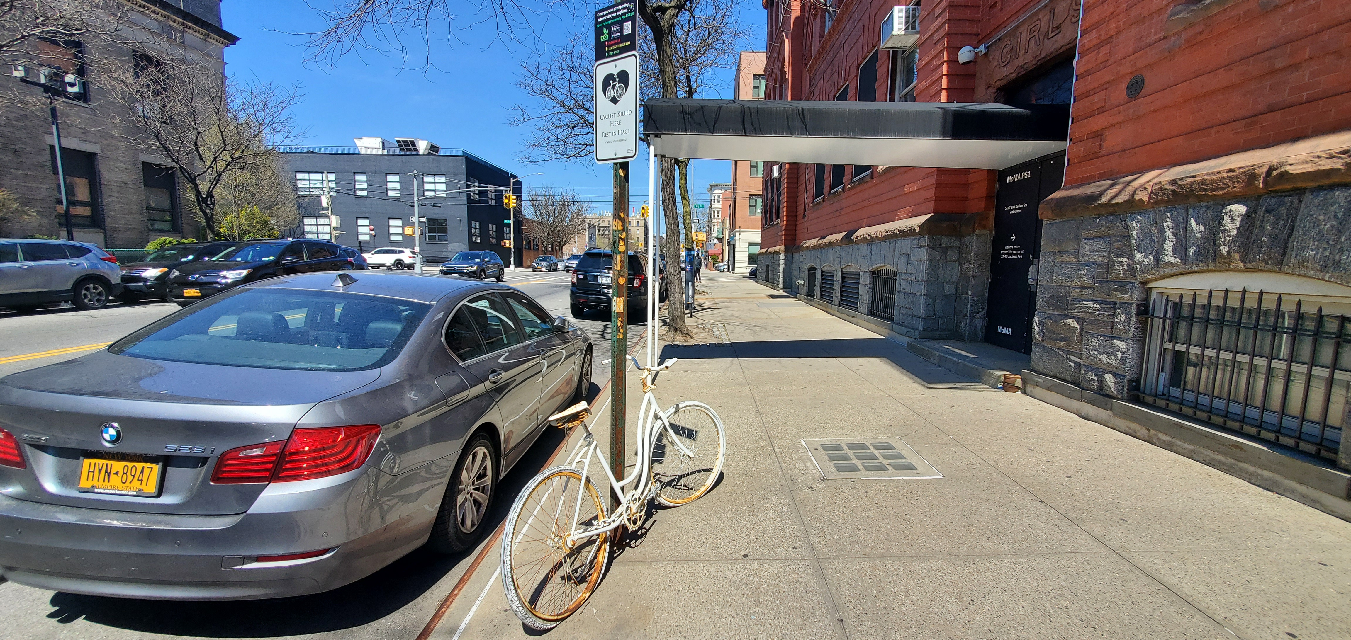 White bike and plaque attached to a street sign, next to parked car