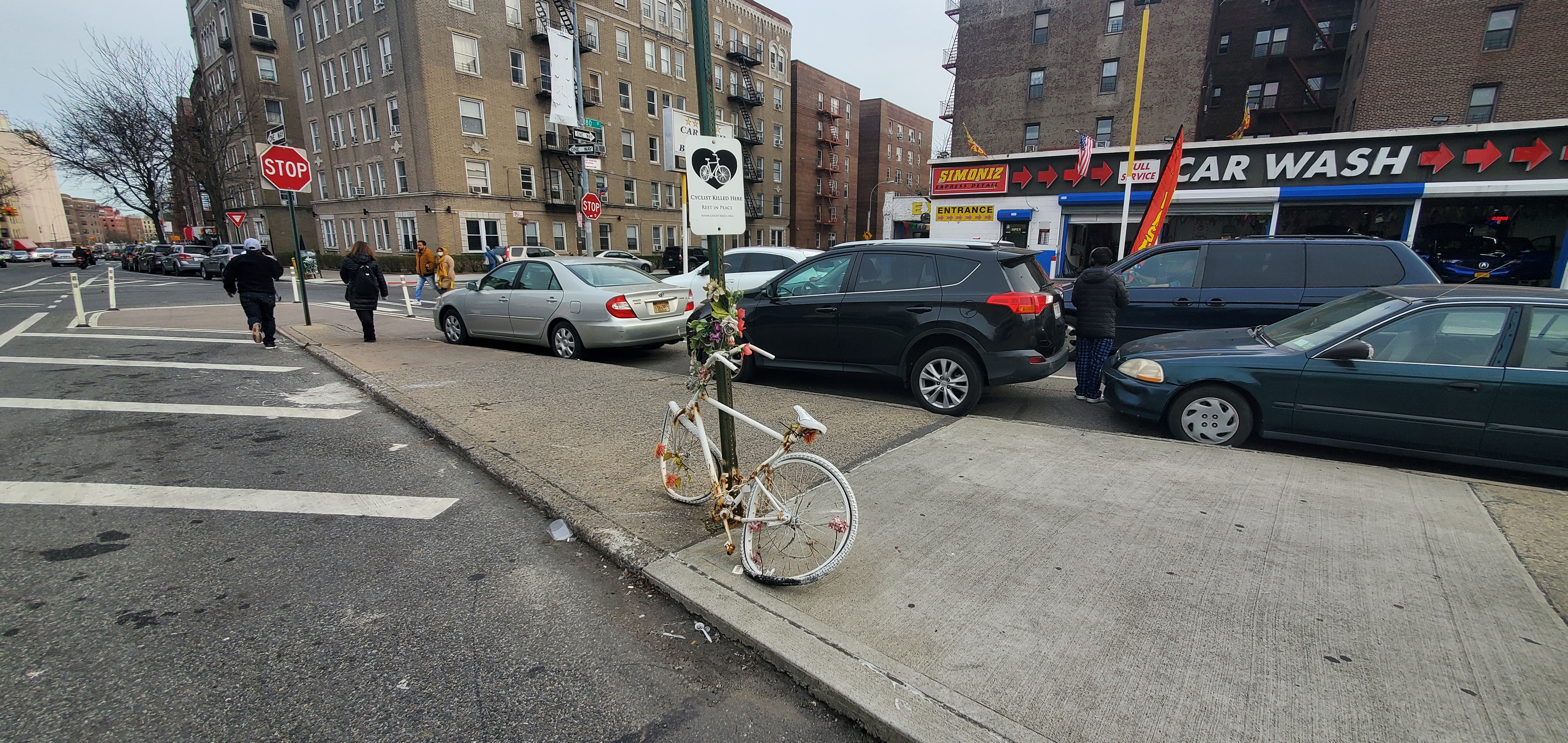 White plaque and white bike decorated with fake flowers chained to street sign in median